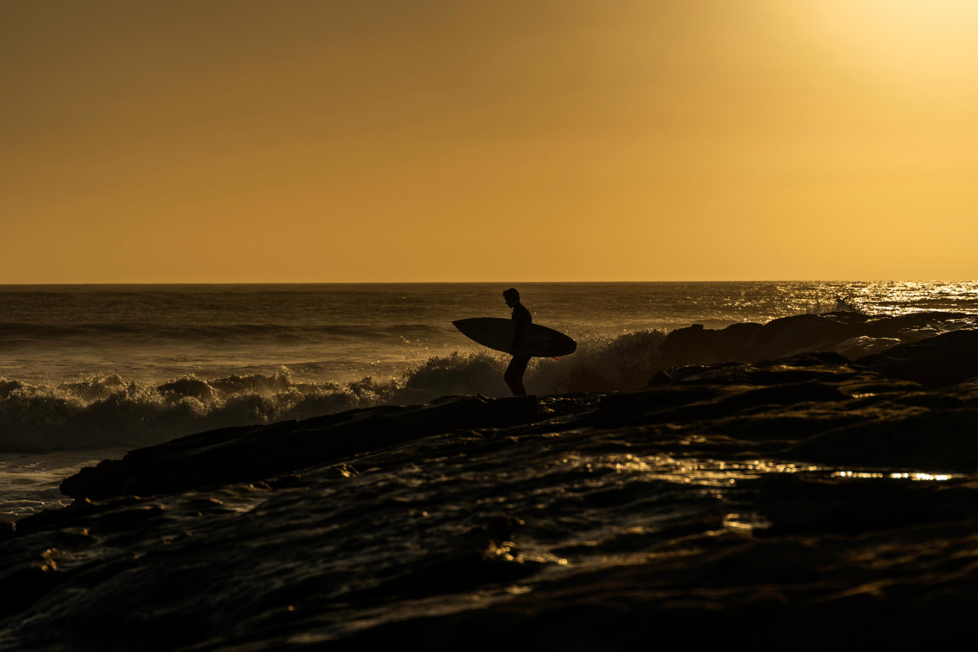 Surfer crossing the rocks at a golden Atlantic sunset
